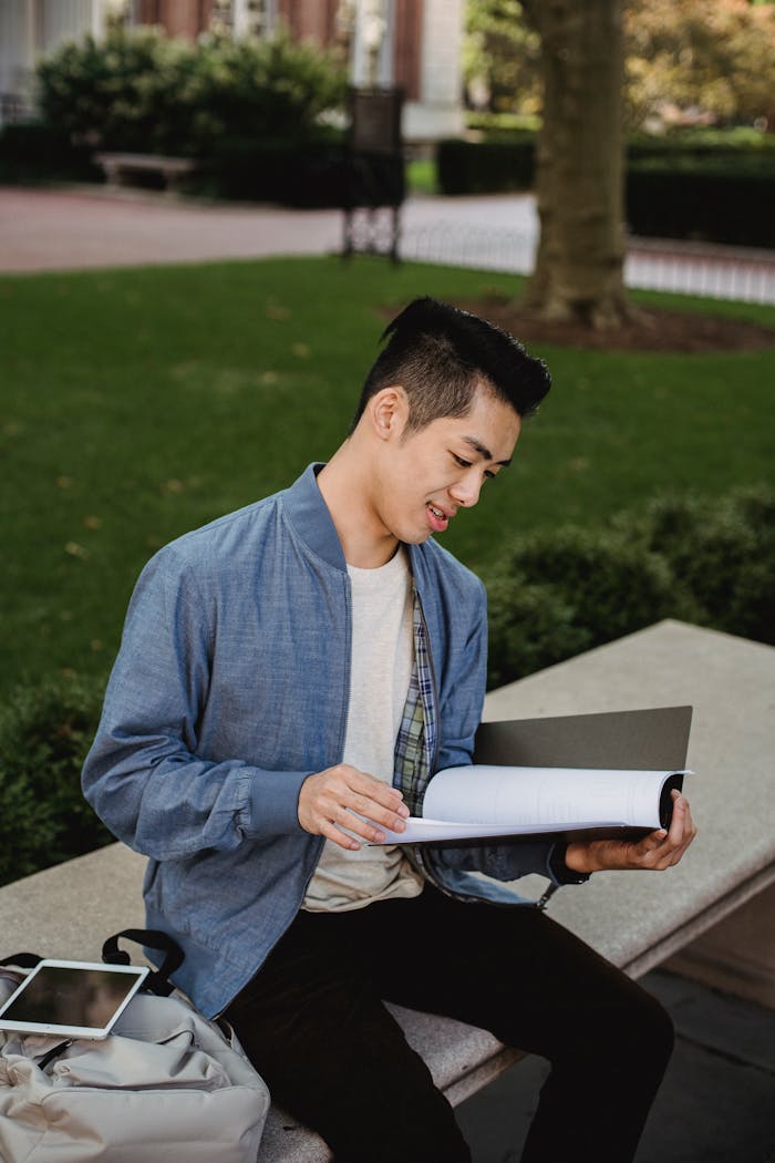 Pensive Asian student reading documents on street